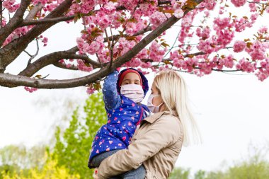 Sokakta yürüyen ve konuşan maskeli bir anne ve kız.