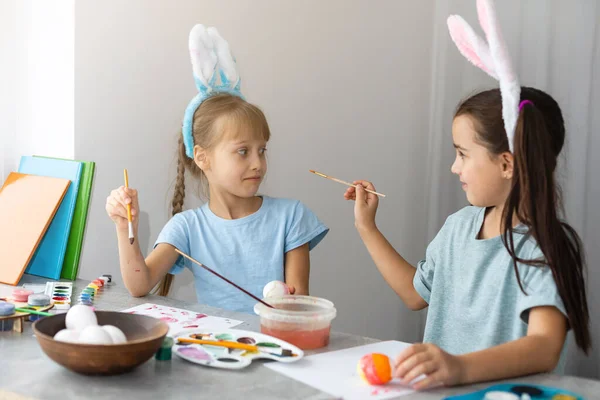 快乐的复活节。两个姐姐在画复活节彩蛋.快乐的家庭孩子为复活节做准备。复活节那天，可爱的小女孩戴着小兔子耳朵. — 图库照片