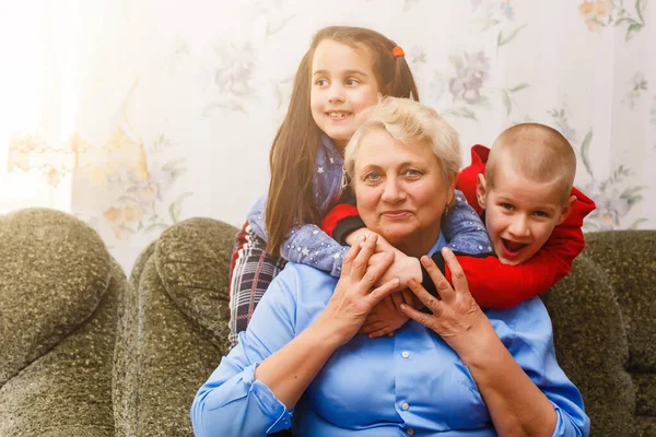 Grandmother and grandchildren sitting together on sofa in living room — Stock Photo, Image
