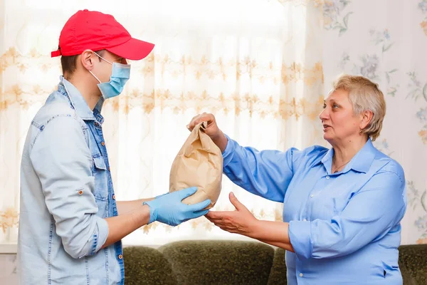 Una anciana se queda en casa. Entrega de comida en una máscara médica. —  Fotos de Stock