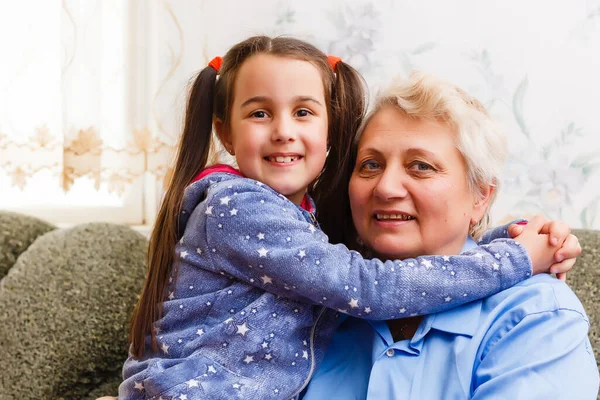 Niña linda y su abuela están pasando tiempo juntos en casa. Divertirse, abrazar y sonreír mientras se sienta en el sofá. —  Fotos de Stock