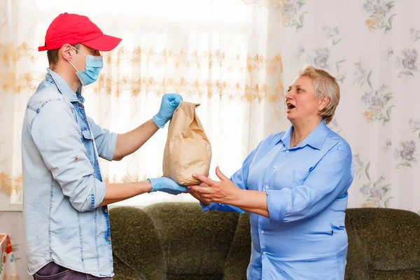 Una anciana se queda en casa. Entrega de comida en una máscara médica. — Foto de Stock