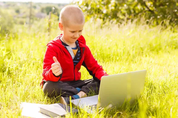 Dálkové studium. Chlapec se učí autopilota. Dělám domácí úkoly na trávě. Dítě se učí na čerstvém vzduchu. Childs ruce a počítač — Stock fotografie