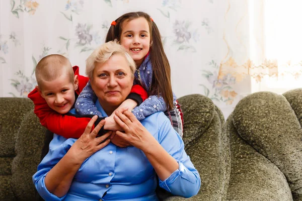 Grandmother and grandchildren sitting together on sofa in living room — Stock Photo, Image