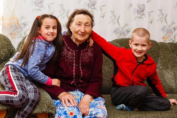 Closeup portrait of happy great-grandmother with great-grandchildren on the sofa at home — Stock Photo, Image