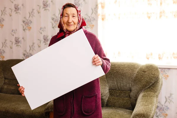 Starsza kobieta trzymająca puste pionowe płótno w rękach. Pusta ramka na tekst lub zdjęcie. kobieta z plakatem makiety — Zdjęcie stockowe