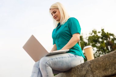 Yazın şehir parkında dizüstü bilgisayarla iş arayan bir kadın.