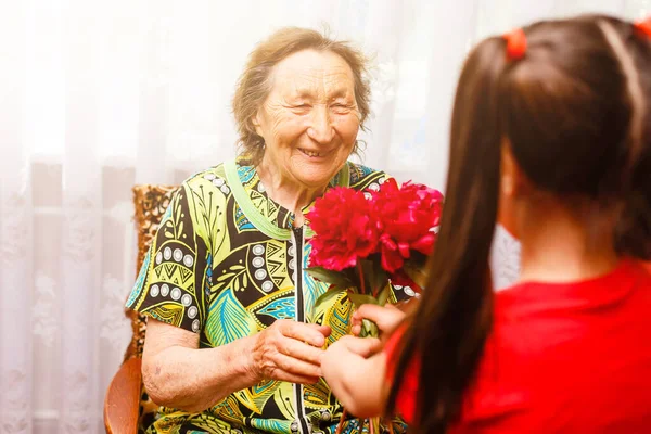 Menina dando a sua bisavó uma flor rosa — Fotografia de Stock