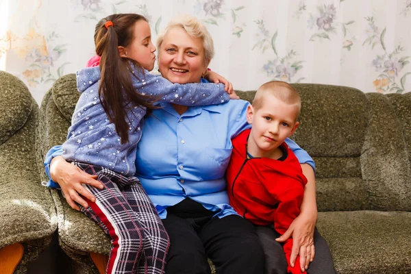 Grootmoeder en kleinkinderen zitten samen op de bank in de woonkamer — Stockfoto