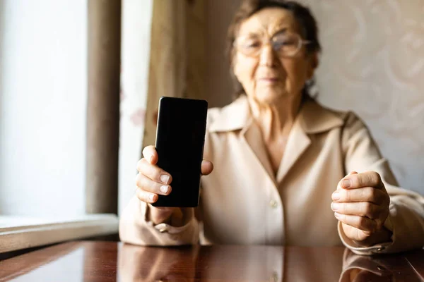 Дуже стара старша кавказька бабуся з глибокими зморшками сидить вдома, використовує свій смартфон на відкритій передній камері для відеодзвінка.. — стокове фото