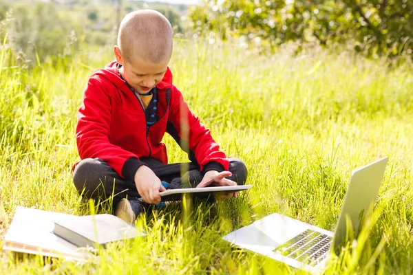 Distance learning. Boy learns autdoor laptop. Doing homework on grass. The child learns in the fresh air. The childs hands and computer