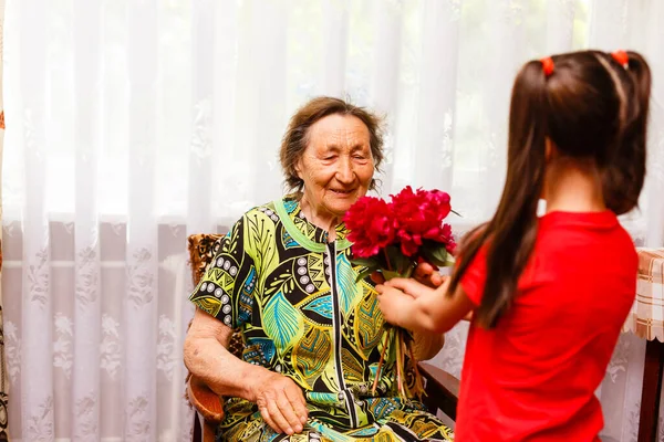 Little girl giving her great grandmother a pink flower — Stock Photo, Image