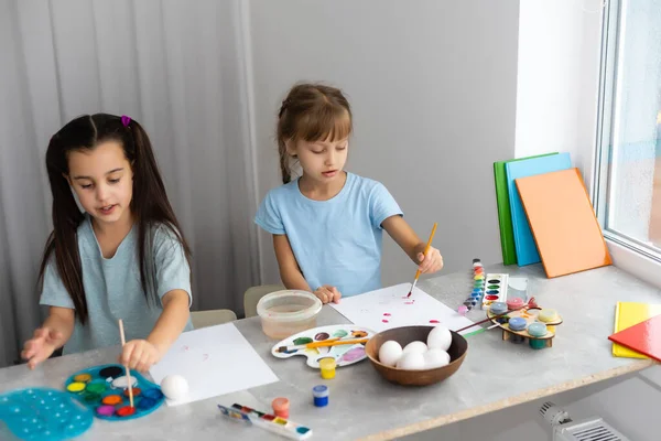 Two happy cute girls sisters paint Easter eggs, oh laugh, show eggs and painted hands — Stock Photo, Image