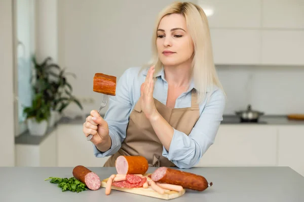 Een mooi meisje weigert worsten op een neutrale achtergrond. Het begrip vegetarisme. — Stockfoto