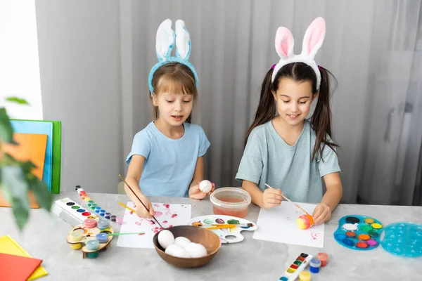 Two happy cute girls sisters paint Easter eggs, oh laugh, show eggs and painted hands — Stock Photo, Image