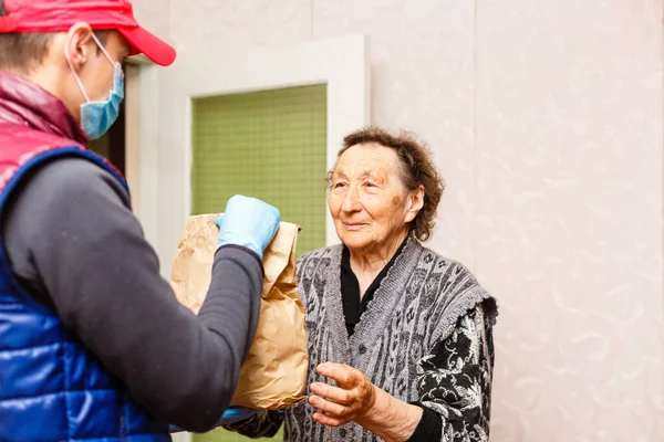 Una anciana se queda en casa. Entrega de comida en una máscara médica a los ancianos. —  Fotos de Stock