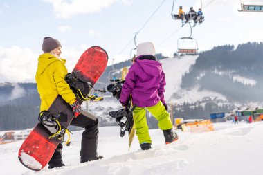 Bir dağ evinde snowboard yapan anne ve kız.