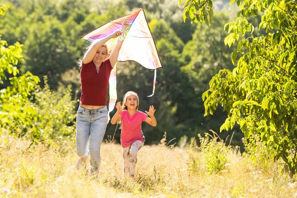 Feliz familia madre e hijo correr en el prado con una cometa en el verano en la naturaleza — Foto de Stock