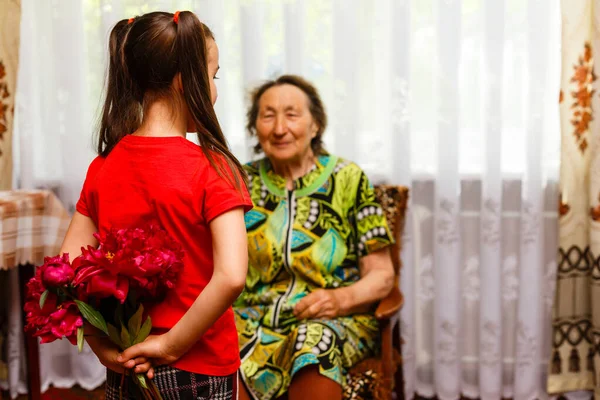 Menina dando a sua bisavó uma flor rosa — Fotografia de Stock