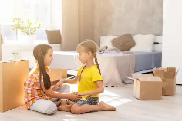 Happy family in living room. Preschool daughters sitting and help unpacking cardboard boxes belongings. Buy real estate, relocation at new modern house