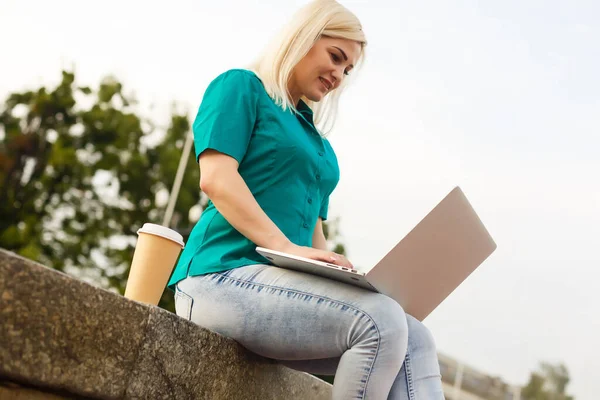 Mulher com laptop no jardim. Negócios on-line ao ar livre. A garota trabalhando remotamente autdoor — Fotografia de Stock