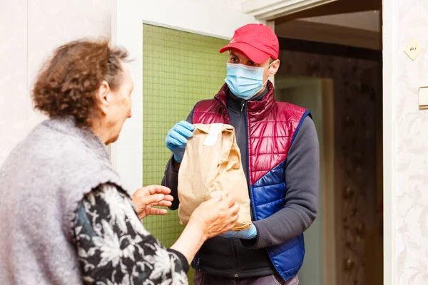 Una anciana se queda en casa. Entrega de comida en una máscara médica a los ancianos. —  Fotos de Stock