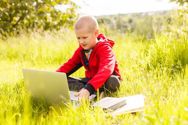 Mladý chlapec s knihami a notebookem na zelené trávě v parku — Stock fotografie