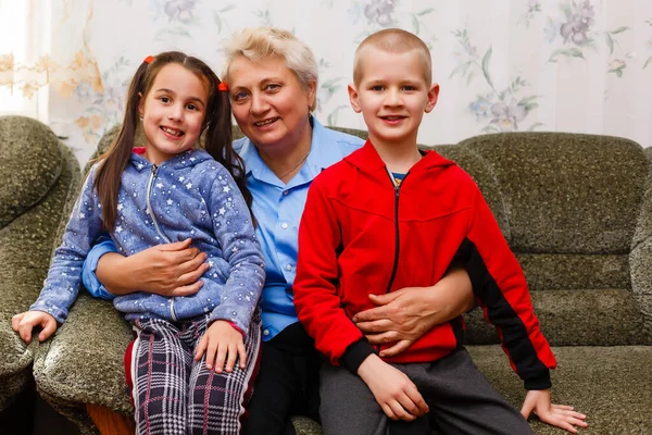 Grootmoeder en kleinkinderen zitten samen op de bank in de woonkamer — Stockfoto