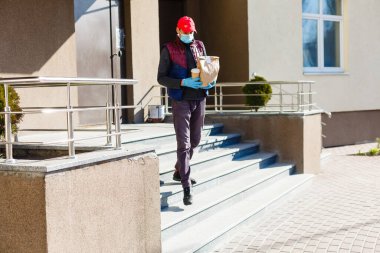 Evin arka kapısında beyaz bir yemek poşeti taşıyan bir teslimatçı. Koruyucu maskeli bir yemek dağıtıcısı.