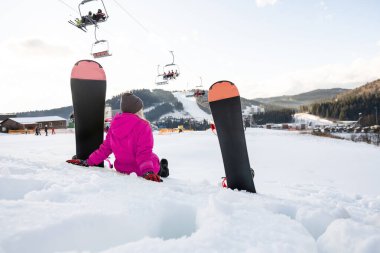 Kışın tatil köyünün yamacında snowboard yapan genç bir kadın.