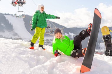 Snowboard yapan anne ve kızı karda oynuyorlar.