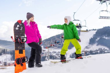 Snowboard yapan anne ve kızı karda oynuyorlar.