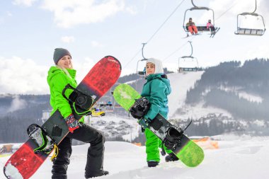 Snowboard yapan anne ve kızı karda oynuyorlar.