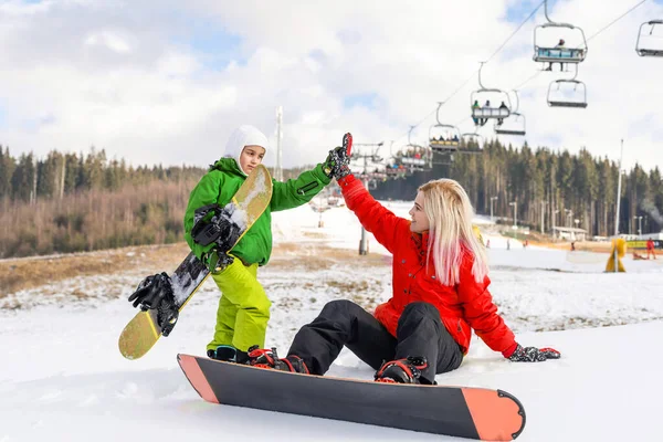 Anne ve kızı kış tatilinde snowboard yapıyor.