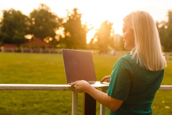 Женщина с ноутбуком в саду. Бизнес онлайн на свежем воздухе. Девочка, работающая за дверью — стоковое фото