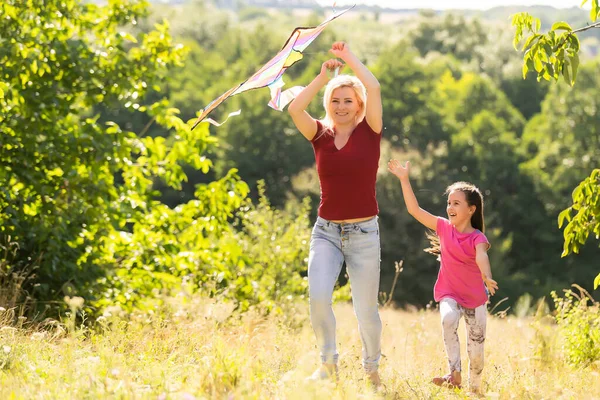 Glückliche Familie Mutter und Kind laufen im Sommer mit dem Drachen auf der Wiese in der Natur — Stockfoto