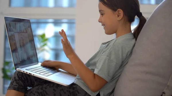 Dziewczynka w wieku szkolnym uczy się w domu. Dziewczyna ogląda lekcję wideo na monitorze laptopa i pisze zadania w notebooku. — Zdjęcie stockowe