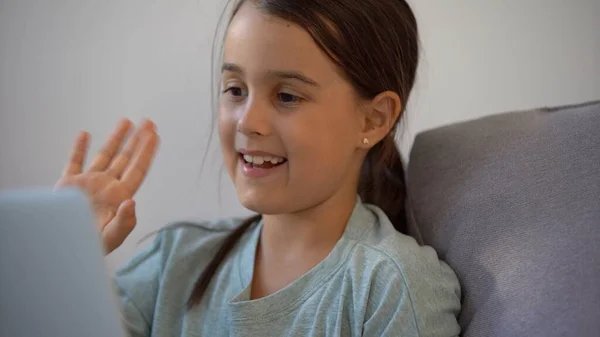 La bambina in età scolare sta studiando a casa. Una ragazza guarda una lezione video su un monitor portatile e scrive attività in un notebook. — Foto Stock