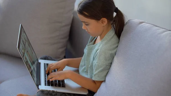 A menina em idade escolar está estudando em casa. Uma menina assiste a uma aula de vídeo em um monitor de laptop e escreve tarefas em um notebook. — Fotografia de Stock