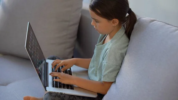 Meisje van school leeftijd studeert thuis. Een meisje kijkt een videoles op een laptop monitor en schrijft taken in een notebook. — Stockfoto