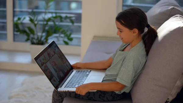 Holčička ve školním věku se učí doma. Dívka se dívá na video lekci na notebooku monitoru a píše úkoly do notebooku. — Stock fotografie