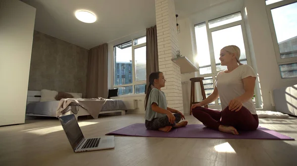 Madre e hija practicando clases de yoga en línea en casa durante la cuarentena durante la pandemia del coronavirus. Familia haciendo deportes juntos en línea desde casa durante el aislamiento juntos en casa — Foto de Stock