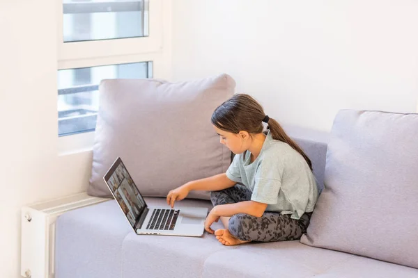 Az iskoláskorú kislány otthon tanul. Egy lány videó leckét néz egy laptop monitoron, és feladatokat ír egy noteszbe.. — Stock Fotó
