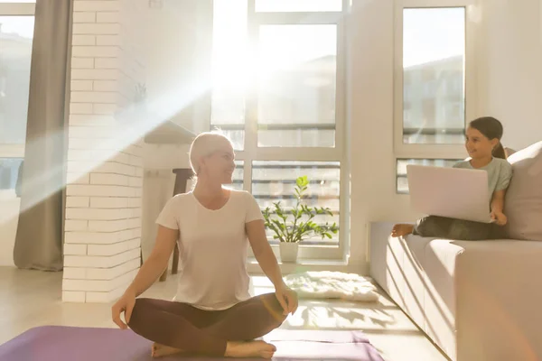 E 'ora dello yoga. Attraente giovane donna che esercita e si siede in posizione loto yoga mentre riposa a casa — Foto Stock