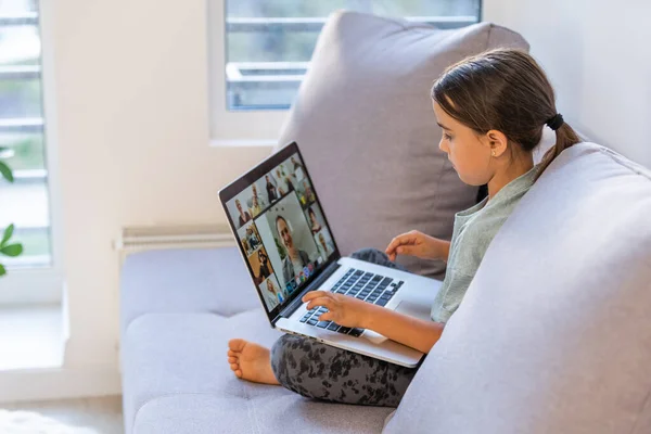 A menina em idade escolar está estudando em casa. Uma menina assiste a uma aula de vídeo em um monitor de laptop e escreve tarefas em um notebook. — Fotografia de Stock