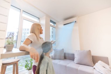Havalandırma altında mutlu bir aile, oturma odasındaki uzaktan kumandalı bir anne kız için konfor ısısını, modern evdeki iklim sistemini ayarlıyor.