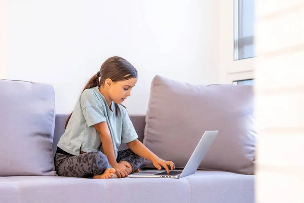Милая маленькая девочка использует ноутбук дома. Образование, онлайн-обучение, домашнее обучение, дистанционное обучение, концепция образа жизни школьниц — стоковое фото