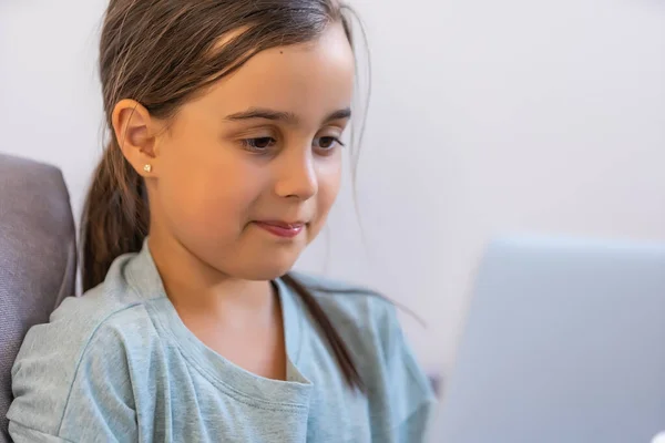 La niña en edad escolar está estudiando en casa. Una chica ve una lección de video en un monitor de computadora portátil y escribe tareas en un cuaderno. — Foto de Stock