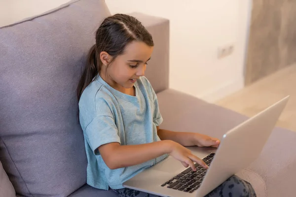 Ragazzina carina che usa il portatile a casa. Istruzione, studio online, studio a casa, apprendimento a distanza, scolaretta concetto di stile di vita dei bambini — Foto Stock