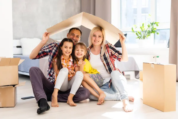 Opgewonden jonge familie veel plezier in de woonkamer uitpakken kartonnen dozen op verhuisdag, gelukkige ouders spelen met kleine dochters springen uit karton pakket, dolblij verhuizen naar een nieuw huis samen — Stockfoto